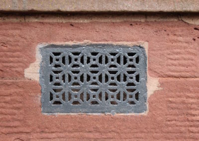 roughly painted grate in the exterior wall, surrounded by red sandstone blocks